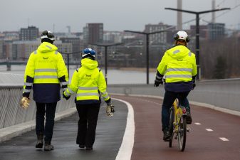 Työmaaväkeä kävelee sillalla kruunut kädessä.